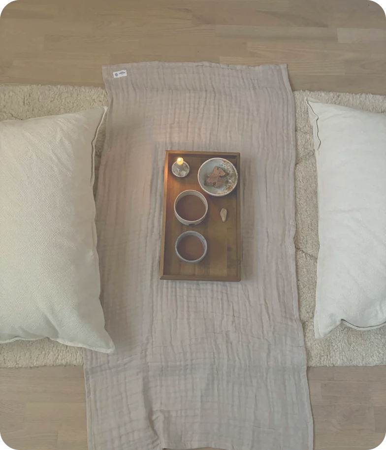 A tray of cacao and a lit candle between two cushions on a soft blanket