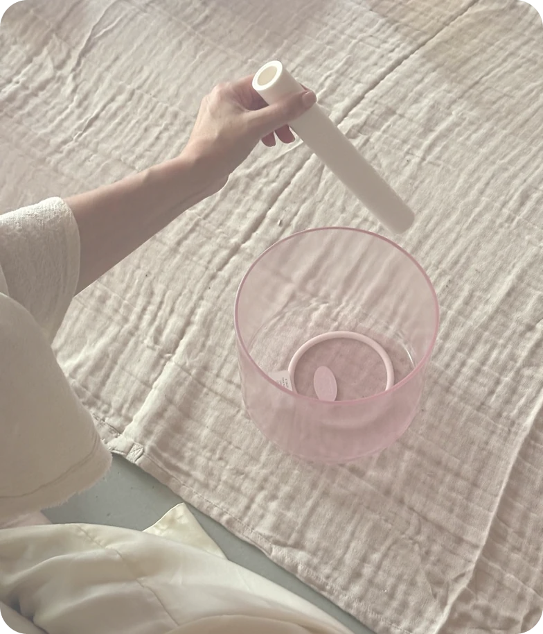 A pink crystal singing bowl being played with a white mallet
