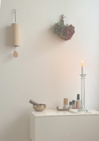 A singing bowl, aromatic oils and a candle beside a Koshi chime and dried flowers