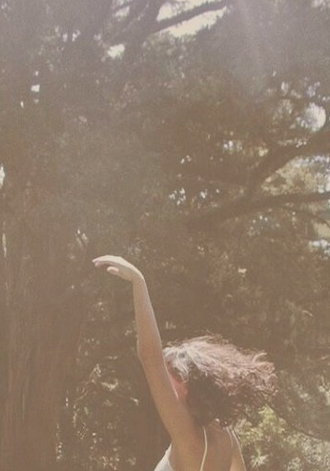 A woman raising her arm gently among sunlit trees