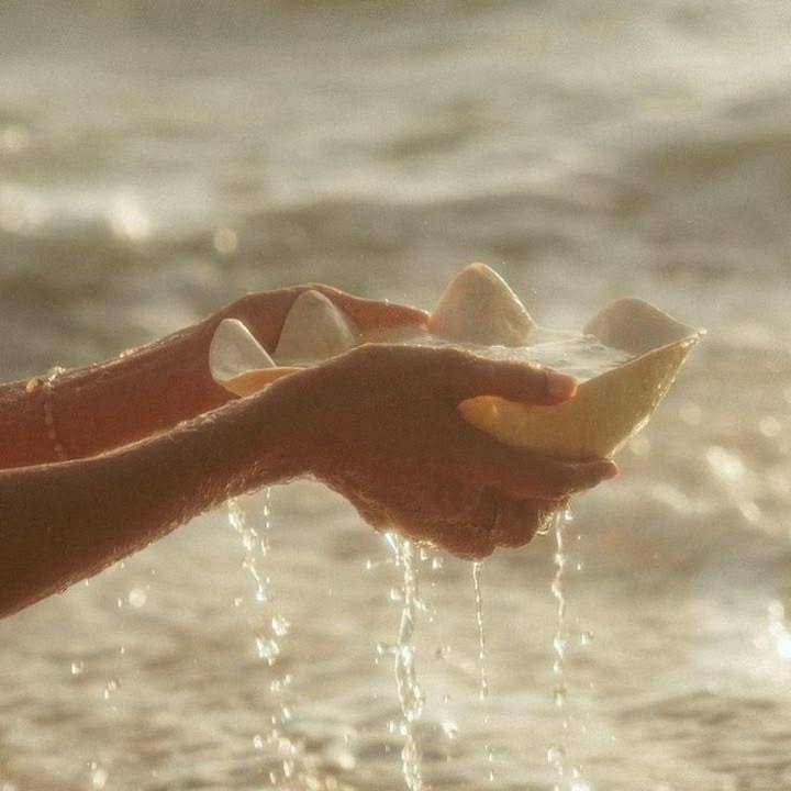 Hands holding crystals in a bowl above sunlit water