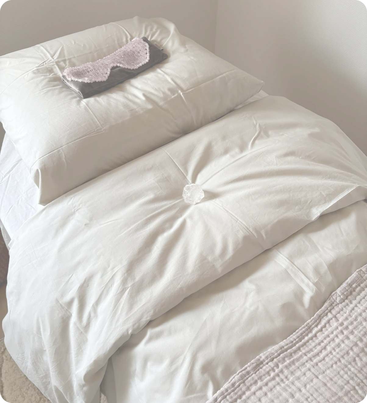 A soft treatment bed with white pillows, a pink eye mask and a clear crystal